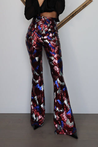 Nadine Merabi geometric sequin flare trousers in burgundy red, blue and silver with a high-waisted fit and statement flared leg silhouette.
