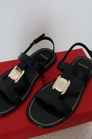 Ferragamo Capri black leather flat sandals in Size 8 featuring gold-tone Gancini hardware, open toes and adjustable slingback straps, displayed on the original red Ferragamo box.