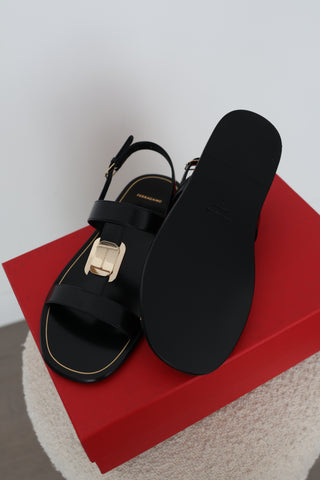 Ferragamo Capri black leather flat sandals in Size 8 featuring gold-tone Gancini hardware, open toes and adjustable slingback straps, displayed on the original red Ferragamo box.