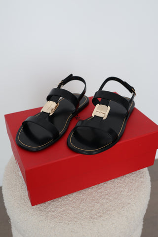 Ferragamo Capri black leather flat sandals in Size 8 featuring gold-tone Gancini hardware, open toes and adjustable slingback straps, displayed on the original red Ferragamo box.