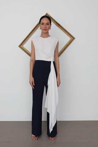 Model wearing a white and navy Carla Zampatti jumpsuit with an asymmetric draped front panel, shown from multiple angles with close-up details of the knot and tailoring.