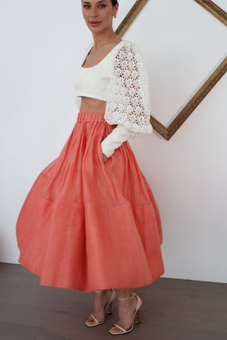 Zimmermann white lace long-sleeve cropped top with structured bodice and voluminous sleeves, worn with coral skirt.