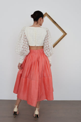 Zimmermann white lace long-sleeve cropped top with structured bodice and voluminous sleeves, worn with coral skirt.