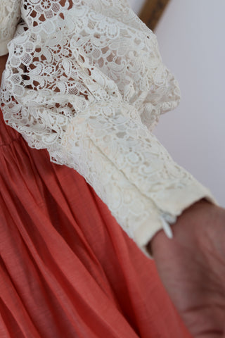 Zimmermann white lace long-sleeve cropped top with structured bodice and voluminous sleeves, worn with coral skirt.