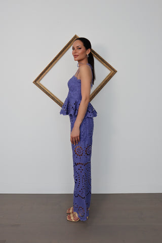 Model wearing Zimmermann violet embroidered linen set with peplum top and flared trousers, standing against white wall with gold tilted frame