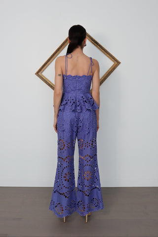 Model wearing Zimmermann violet embroidered linen set with peplum top and flared trousers, standing against white wall with gold tilted frame