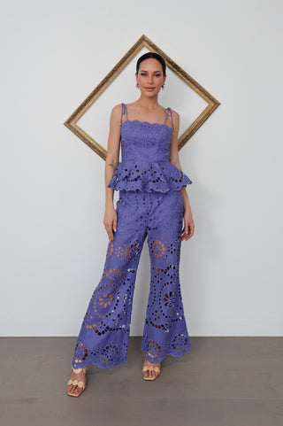 Model wearing Zimmermann violet embroidered linen set with peplum top and flared trousers, standing against white wall with gold tilted frame