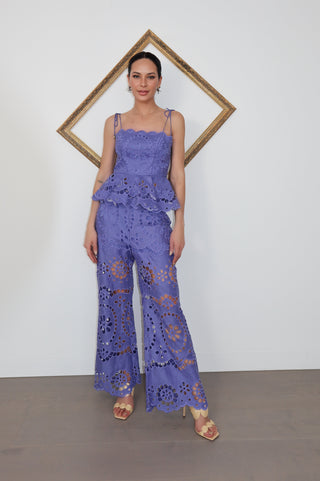 Model wearing Zimmermann violet embroidered linen set with peplum top and flared trousers, standing against white wall with gold tilted frame