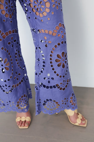 Model wearing Zimmermann violet embroidered linen set with peplum top and flared trousers, standing against white wall with gold tilted frame