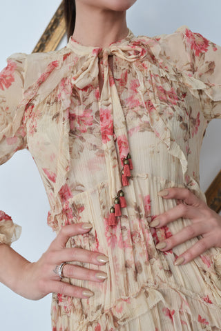 Model wearing Zimmermann floral midi dress in neutral tones with pink flowers, standing against a white background with a tilted gold frame.